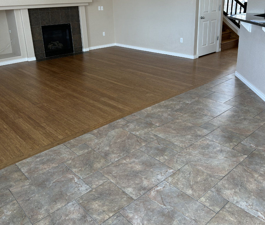 Empty living room with hardwood floors and adjacent kitchen with slate tile